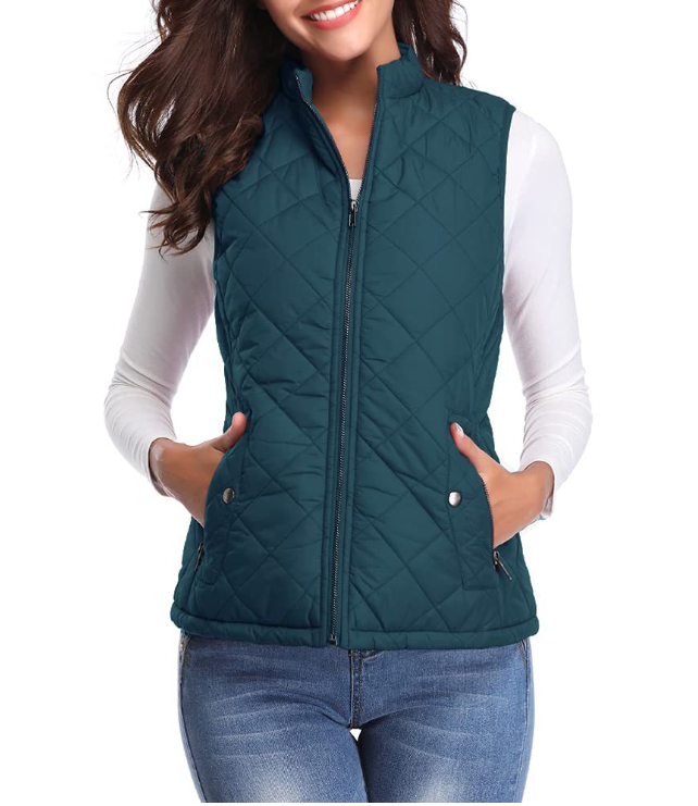 Deep teal diamond-quilted zip-up vest with a stand collar and snap-closure side pockets, styled over a white long-sleeve shirt.