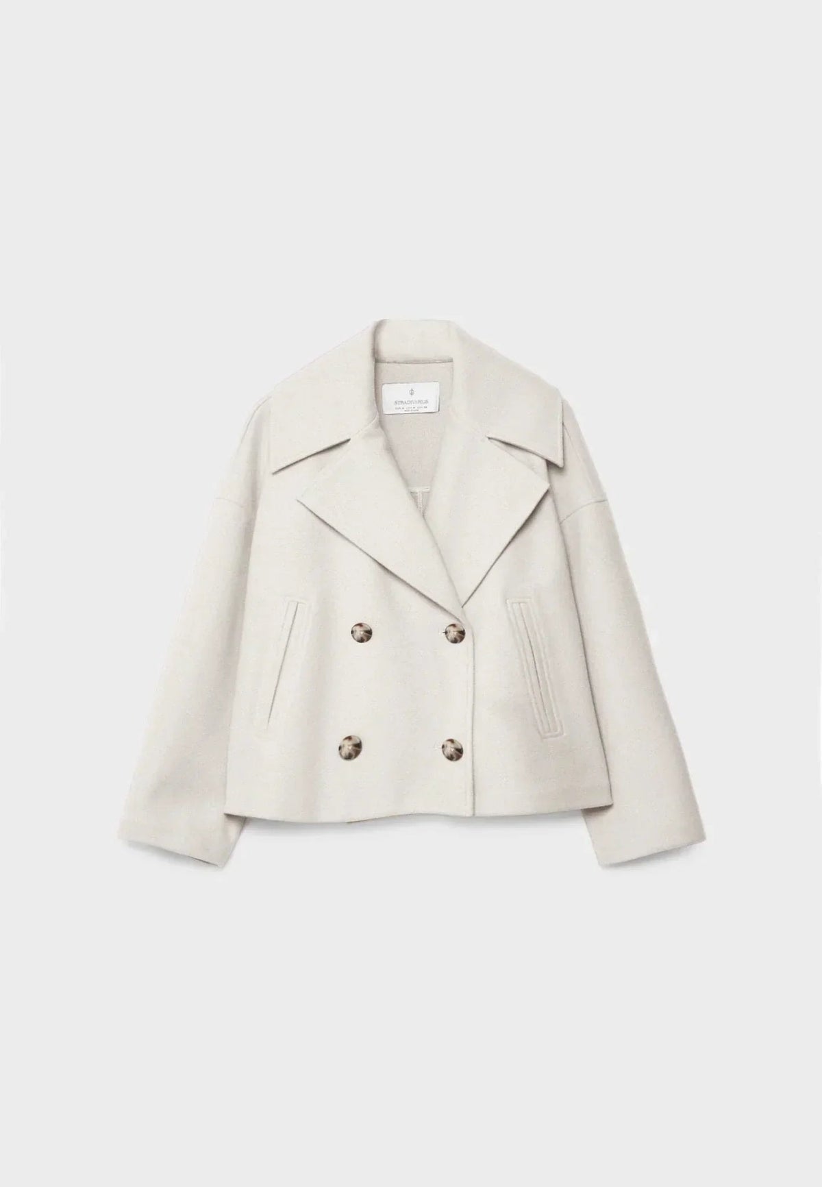 Front view of a cream cropped jacket with wide notched lapels, four buttons, long sleeves, and slanted front pockets.