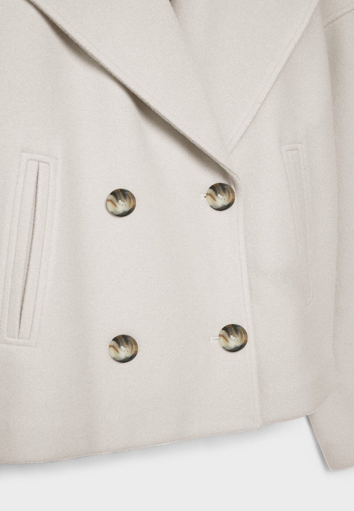 Close-up of the cream jacket showing four shiny buttons, a wide lapel edge, and a slanted front pocket.