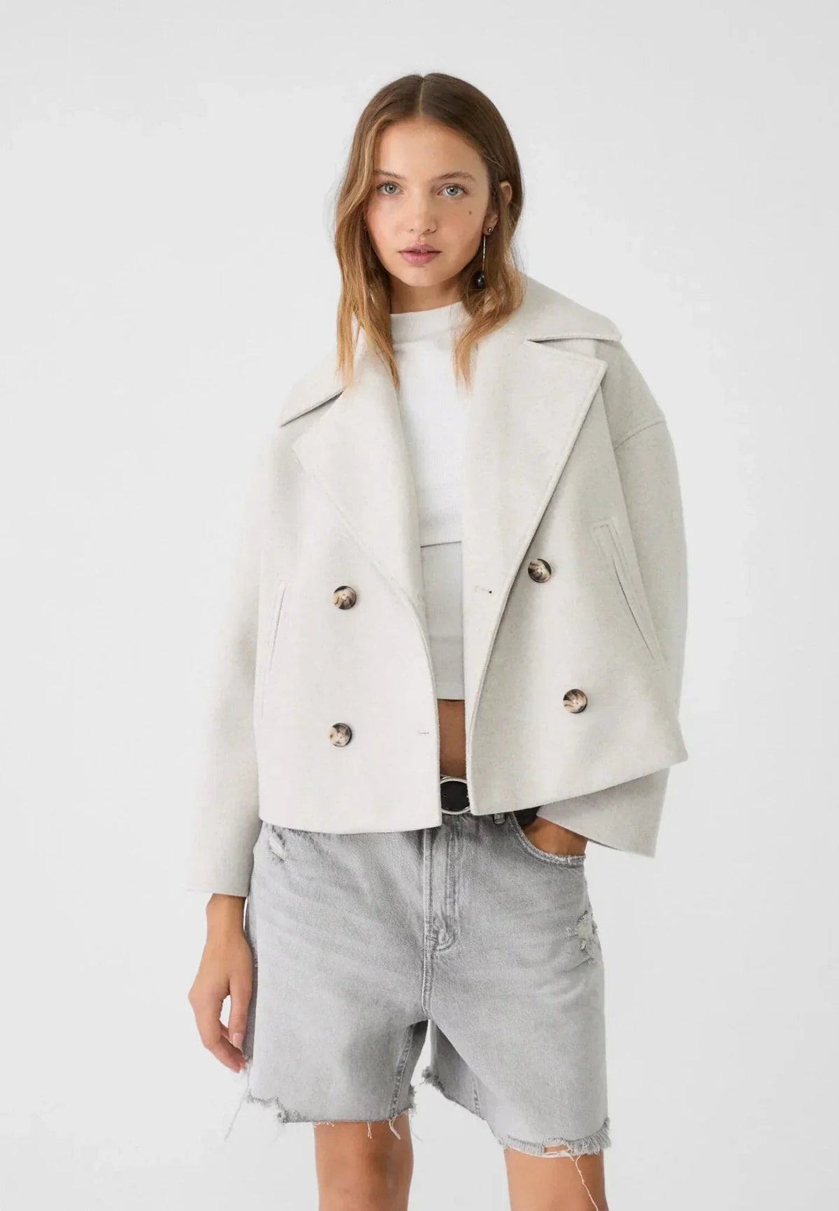 Model wearing the cream double-breasted cropped jacket with gray denim shorts, showing its shorter silhouette and open lapels.