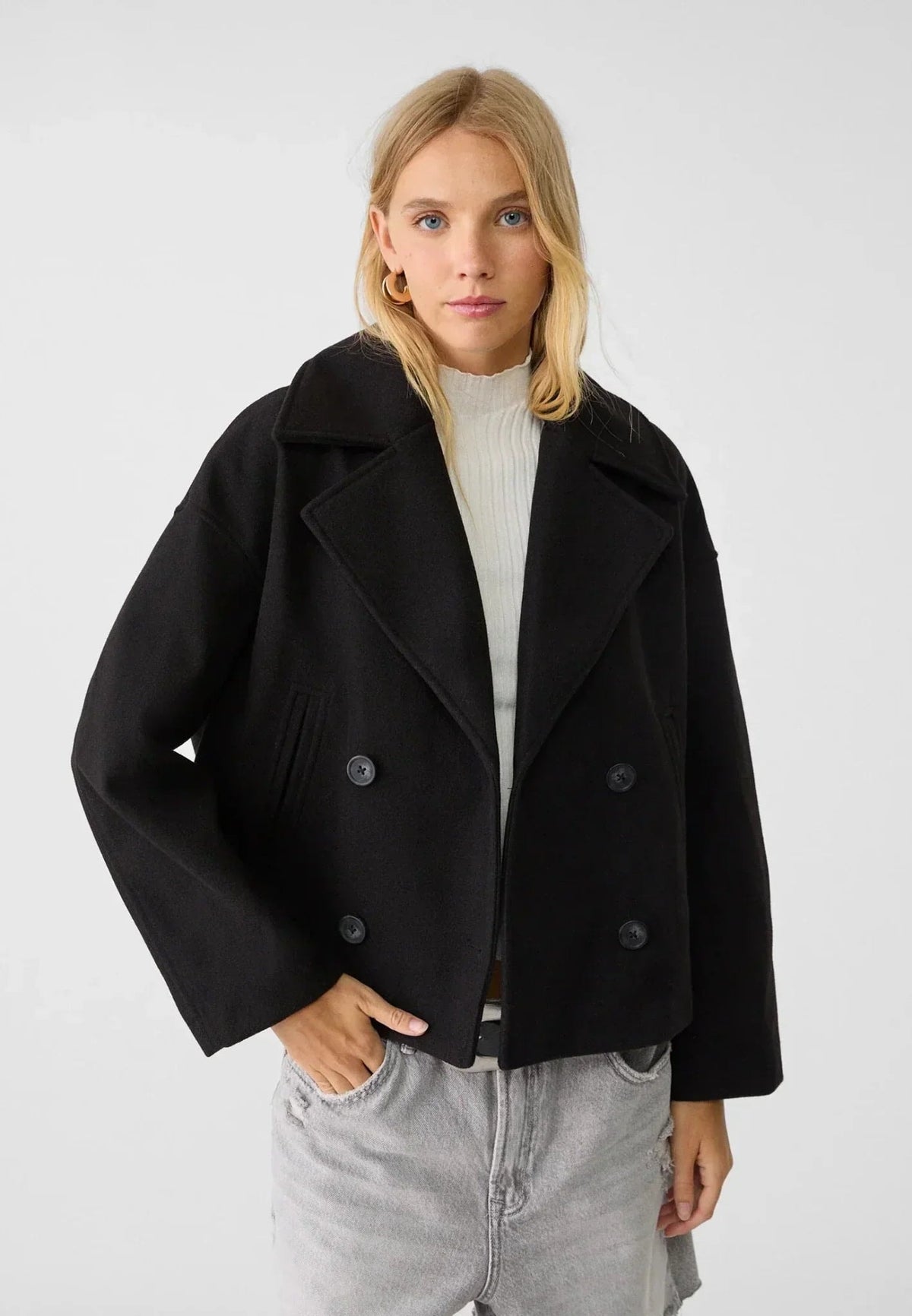 Model wearing the black cropped jacket over a light sweater and gray jeans, with the double-breasted front visible.