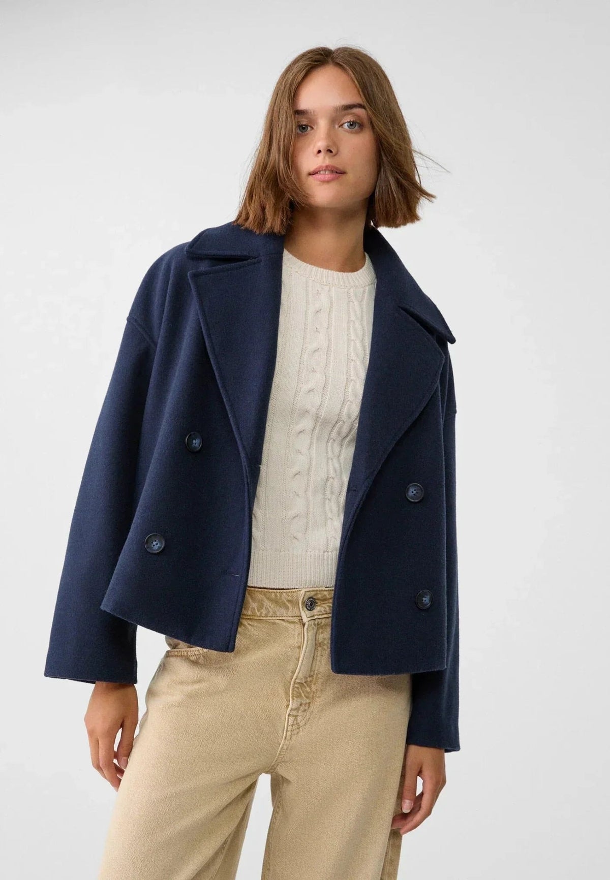 Model wearing the navy cropped jacket over a textured light sweater and beige trousers, showing the tailored shape.