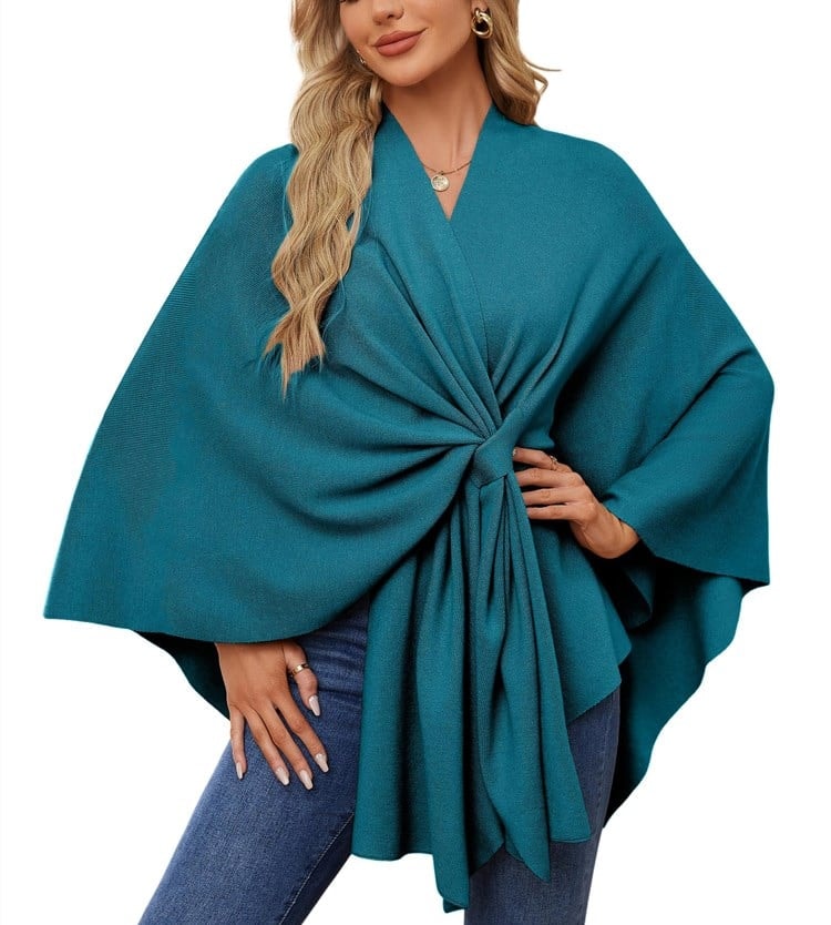 Teal draped tie-front poncho wrap with wide sleeves and an asymmetrical hem, styled with jeans.