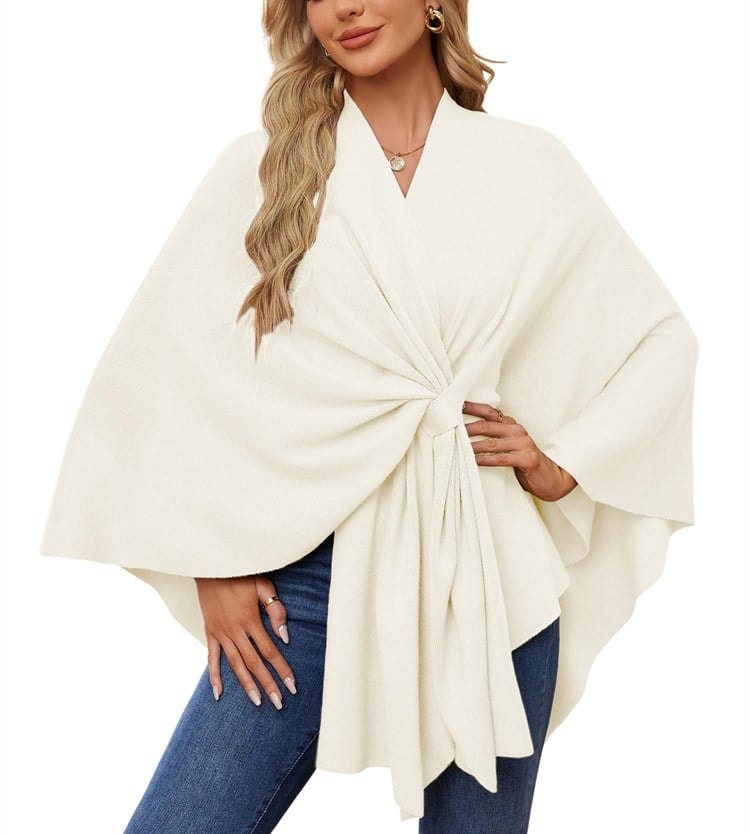 White poncho wrap with a flowing front drape, broad sleeves, and an uneven lower edge.