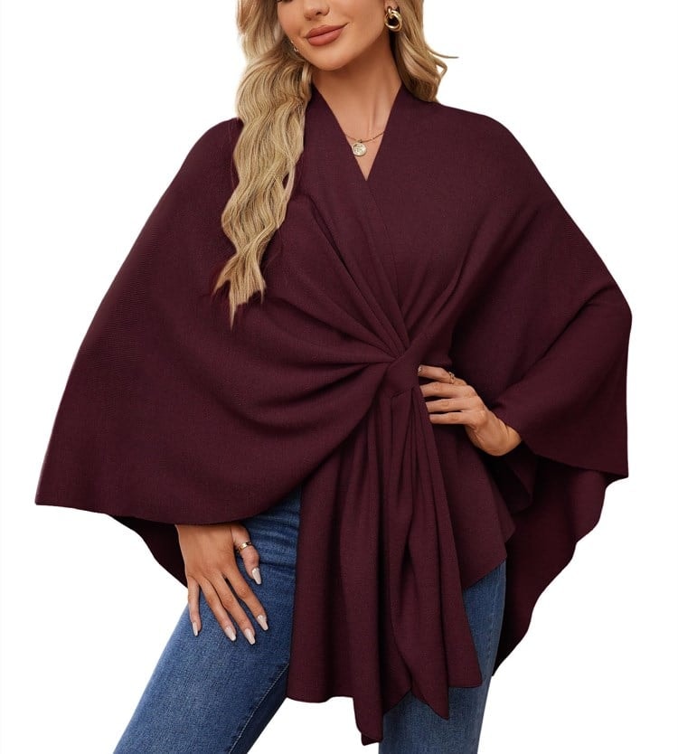 Dark burgundy tie-front poncho wrap layered over jeans with a sweeping side drape.