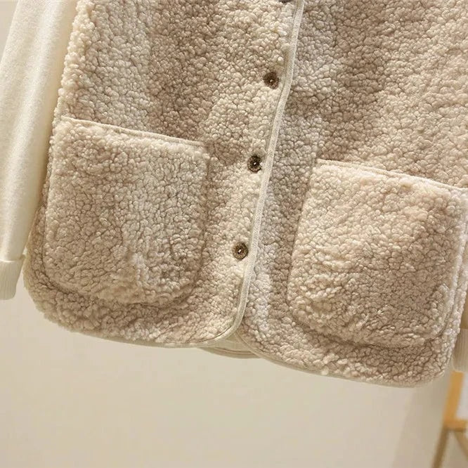 Close-up of the cream fleece vest’s lower front, showing the central buttons, rounded edging and two textured patch pockets.