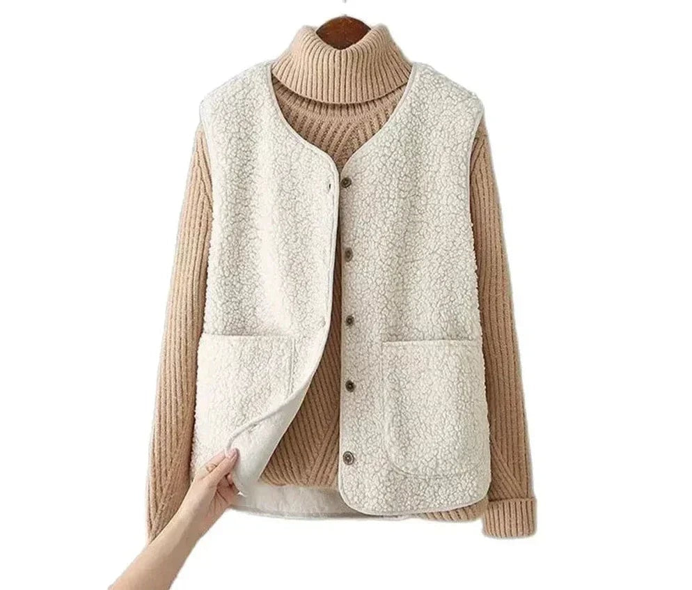 Cream fleece vest displayed over a tan turtleneck sweater against a white background, showing its sleeveless cut and rounded lower edges.