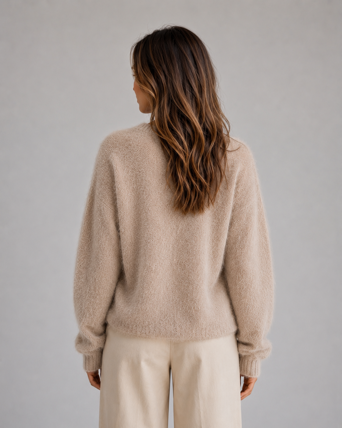 Back view showing the cardigan’s fluffy beige texture, relaxed shape, long sleeves, and ribbed cuffs.