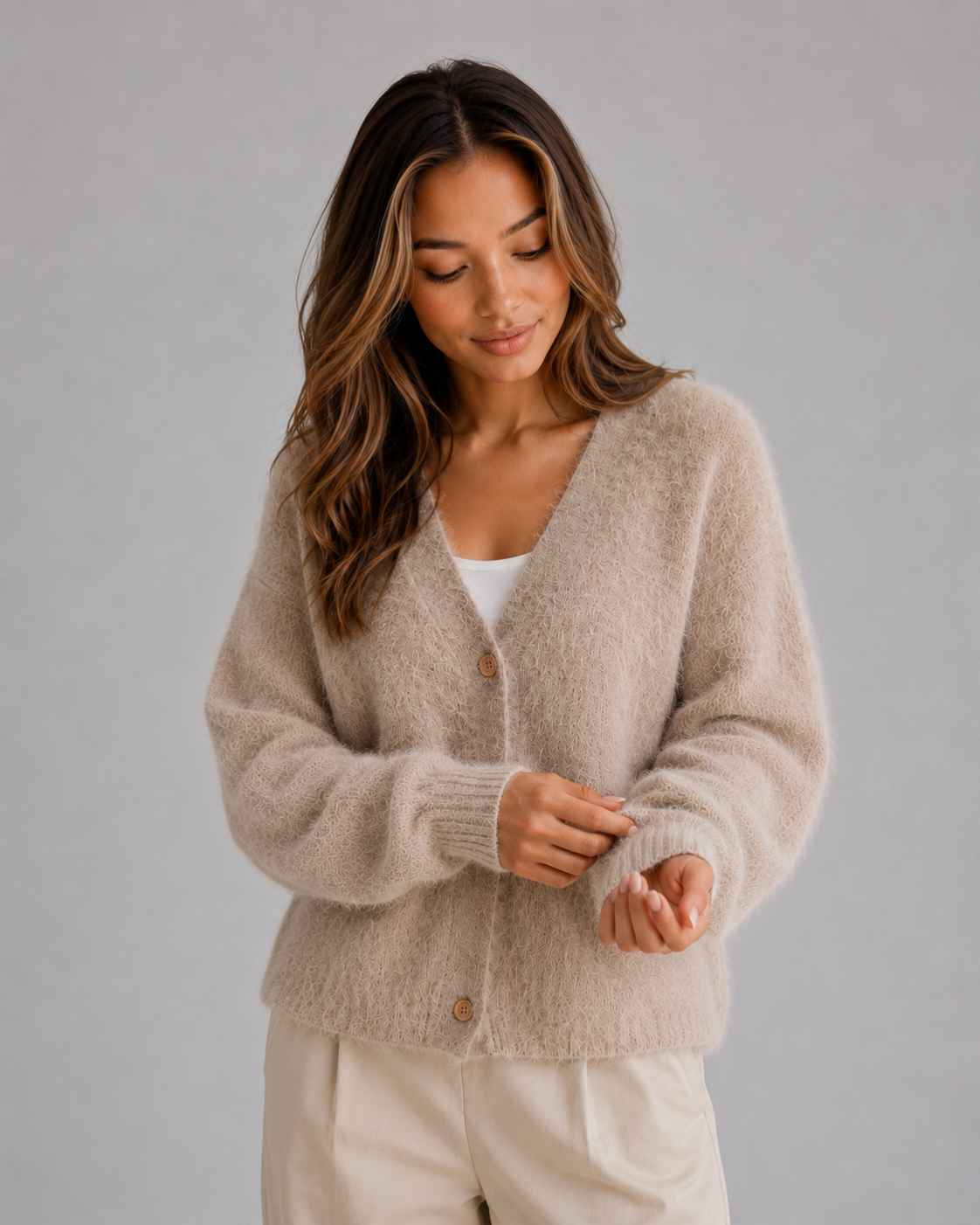 Beige fluffy cardigan worn fastened at the front while the wearer adjusts a ribbed sleeve cuff.