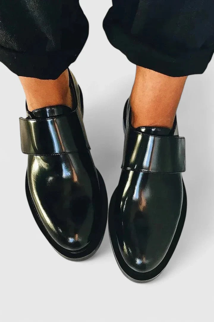Pair of glossy black loafers shown from above on feet, highlighting their rounded almond toes and wide instep straps.