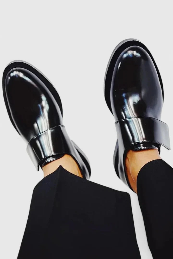 Glossy black strap loafers viewed from the side and above, showing the slip-on design, structured instep bands, and low-profile soles.