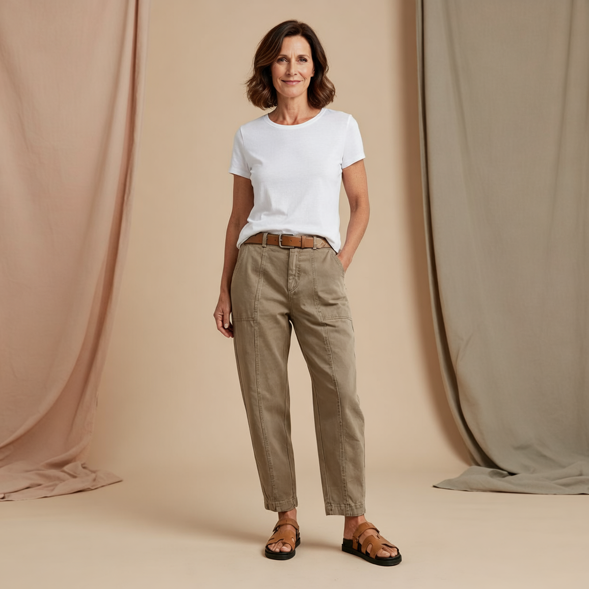 Front view of taupe high-waist tapered utility pants with a brown belt, ankle-length legs, and visible front pockets.