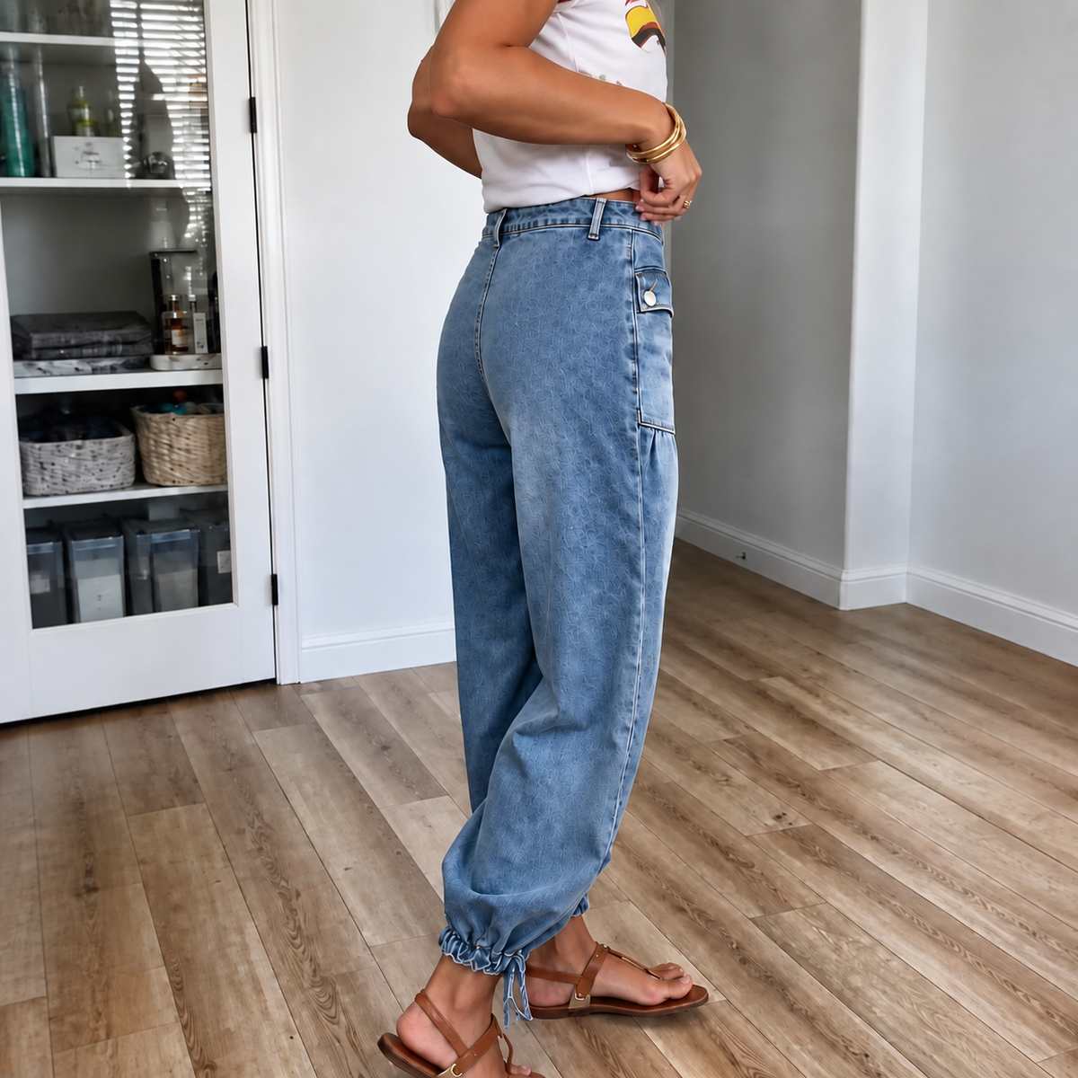 Side view of blue high-waisted barrel leg jeans showing the curved silhouette, side cargo pocket, and tied ankle hems.