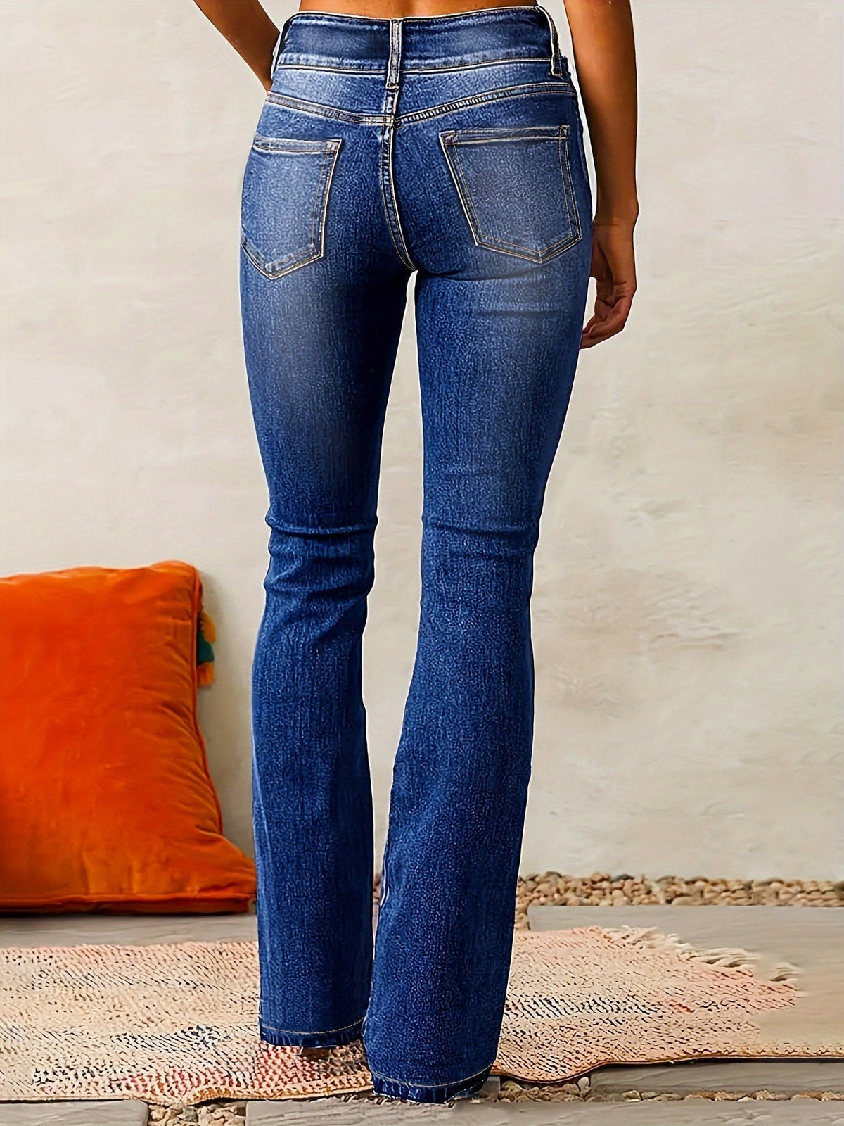 Back view of dark blue high-waisted flared jeans highlighting the rear waistband, belt loops, and two outlined back pockets.
