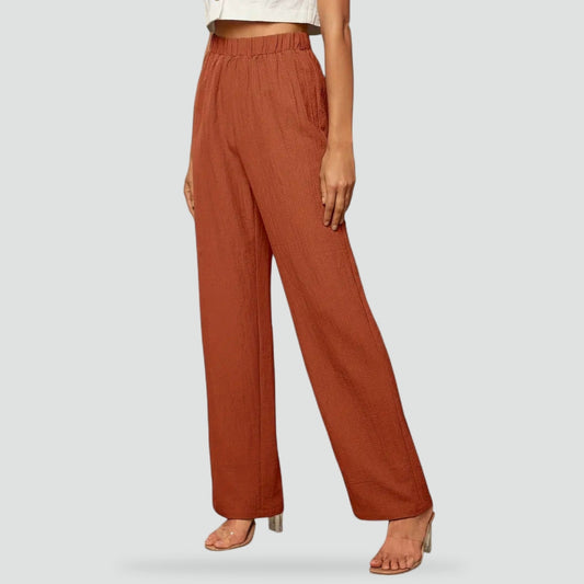 Rust high-waisted straight-leg trousers shown from the front with an elasticated waistband, side pockets, and full-length hems.