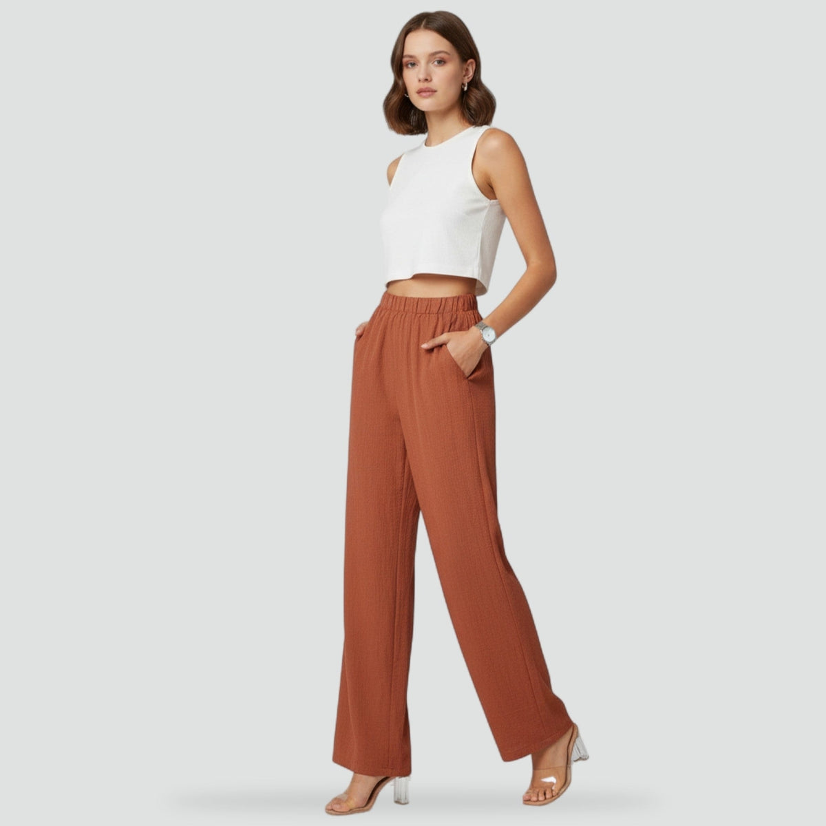 Model wearing rust straight-leg trousers with both hands in the side pockets, showing the high waist and full-length silhouette.