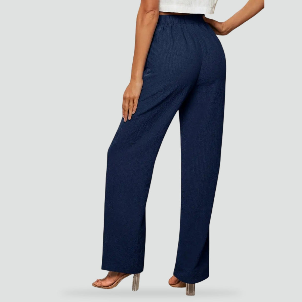 Back view of navy high-waisted trousers with a flexible waistband and straight legs ending above the heels.