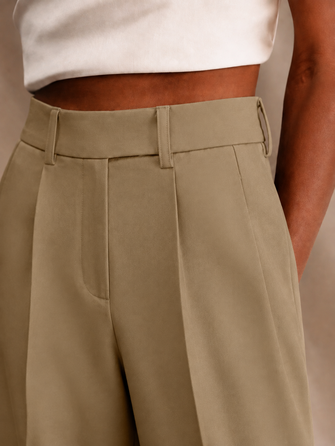 Close-up of light khaki trousers with a high waistband, multiple belt loops, and sharply defined front pleats.
