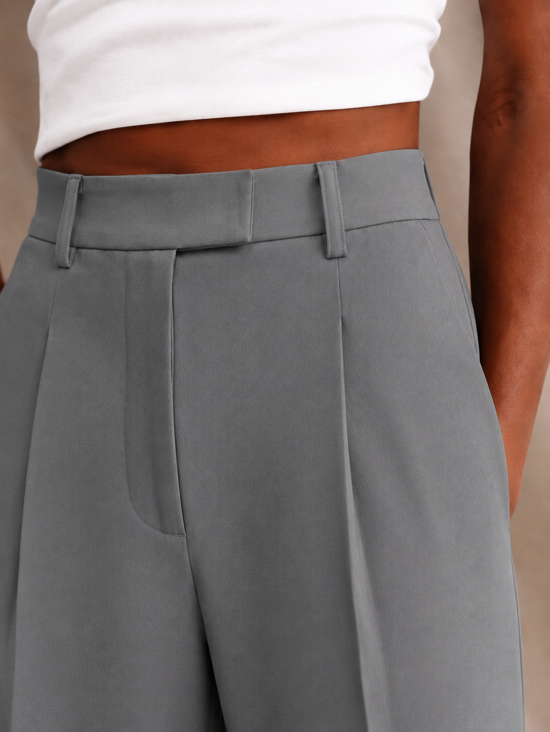 Close-up of gray trousers highlighting the waistband, belt loops, front pleat, and wide upper leg.