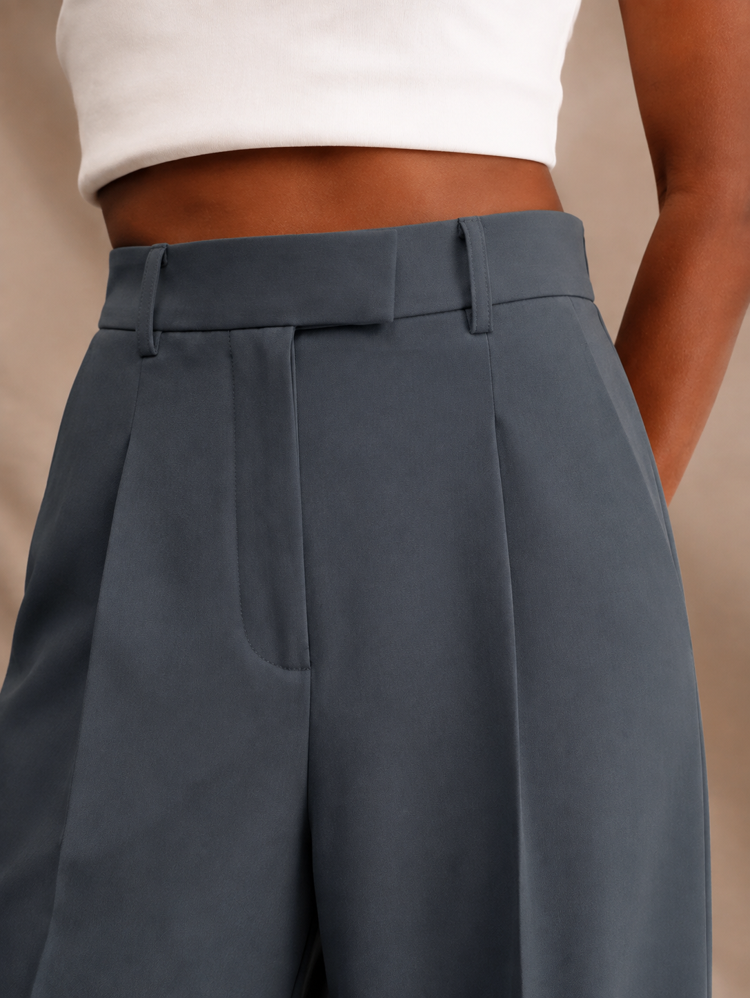 Close angled view of slate-blue trousers showing the high waistband, center belt loop, front pleat, and side pocket.