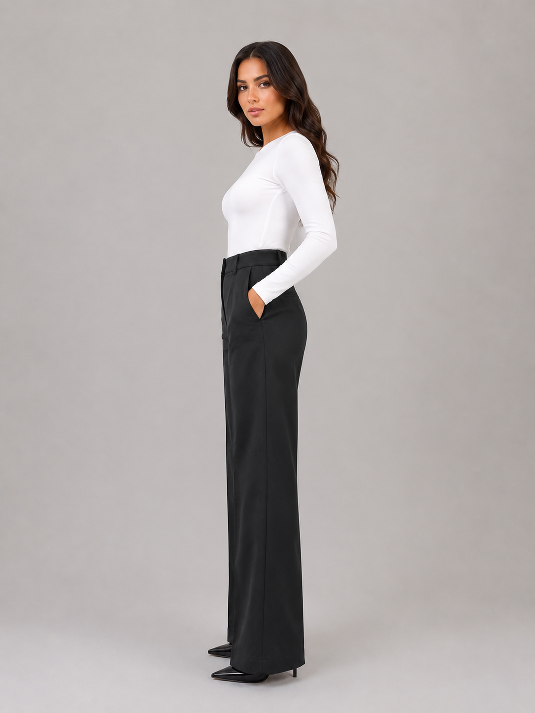 Side profile of black high-waisted wide-leg trousers, highlighting the streamlined tailored silhouette and side pocket.