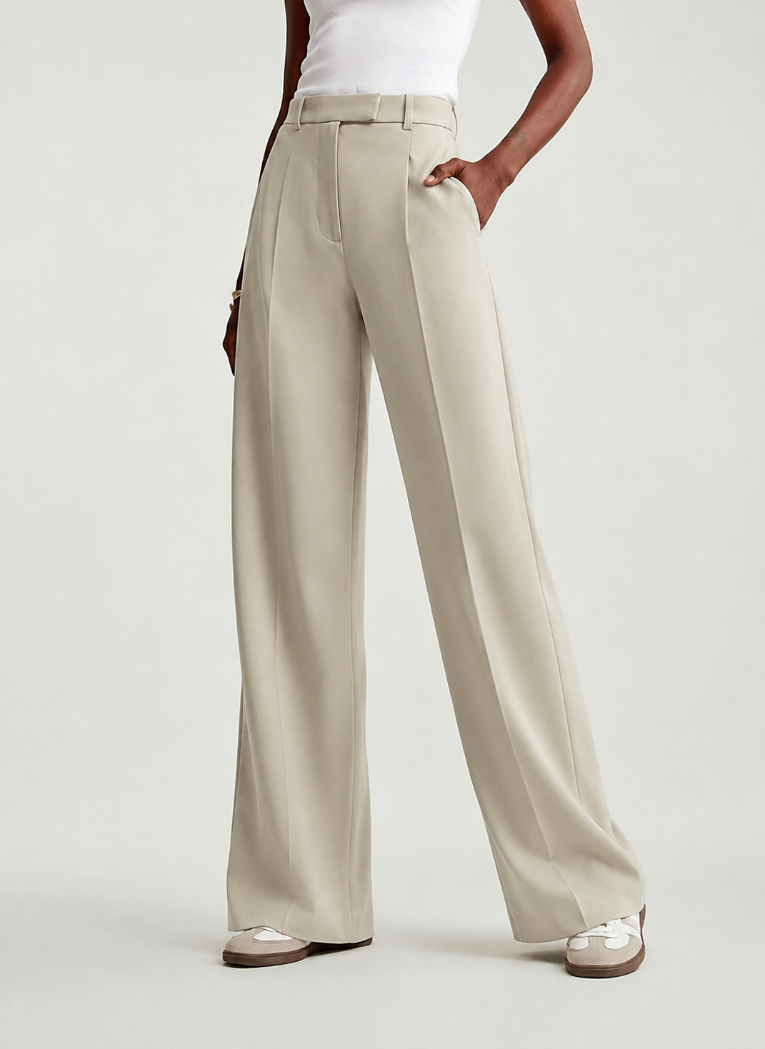 Angled view of beige wide-leg trousers showing a hand in the side pocket and the relaxed drape through the legs.