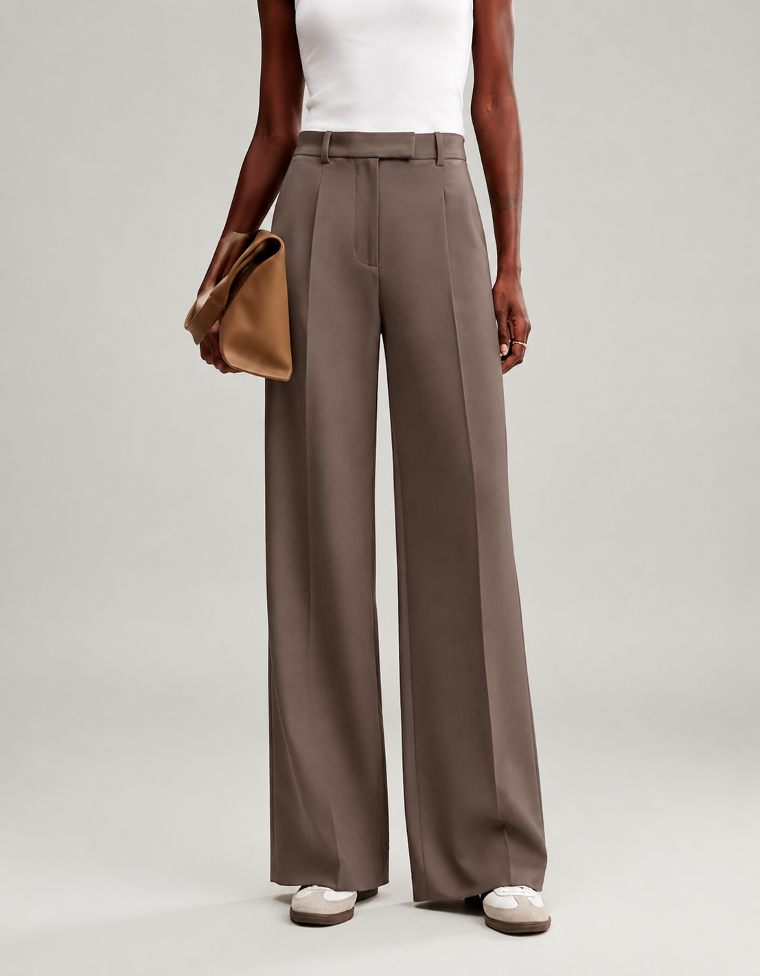 Full-length view of taupe wide-leg trousers styled with a white top and a tan clutch.