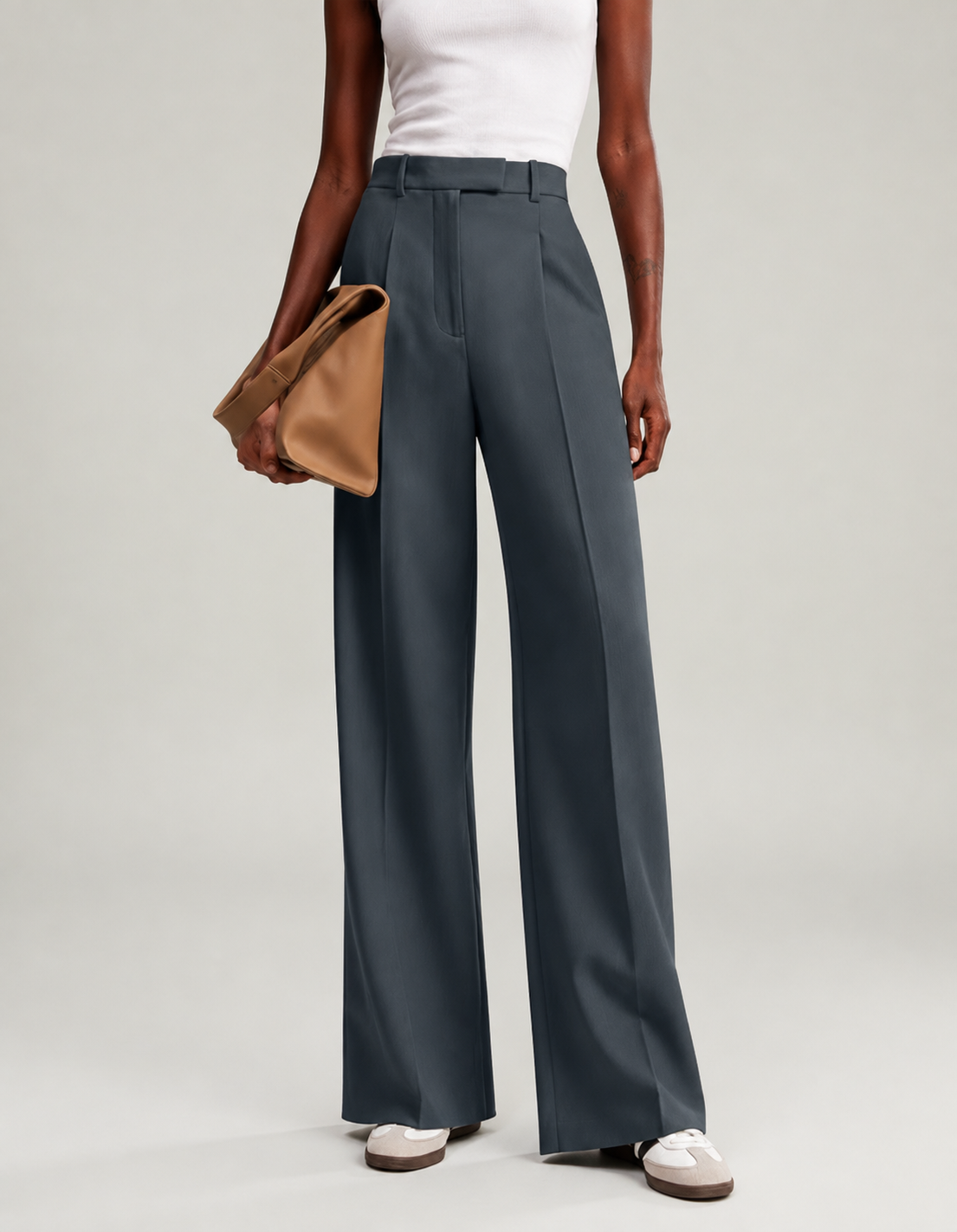 Full-length view of dark slate wide-leg trousers styled with a white top and a tan clutch.