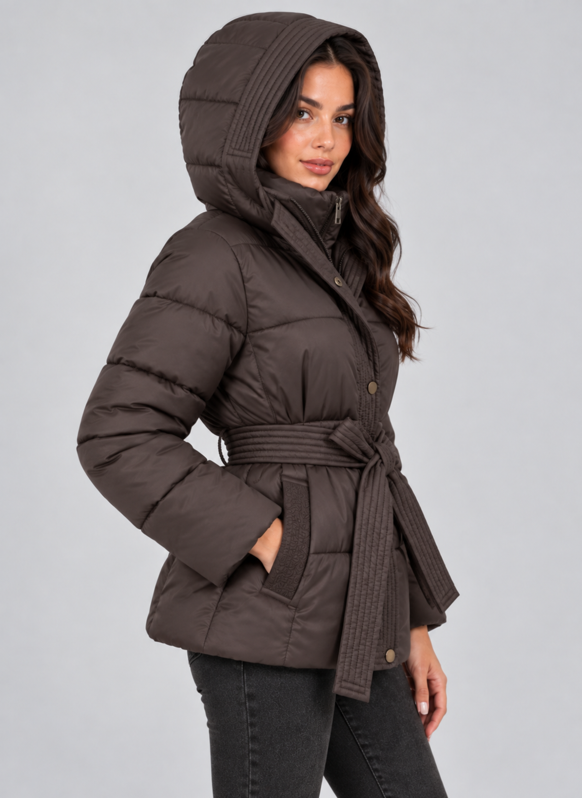 Three-quarter side view of the brown belted puffer jacket worn with the hood up, highlighting the side pocket and layered hood and collar.