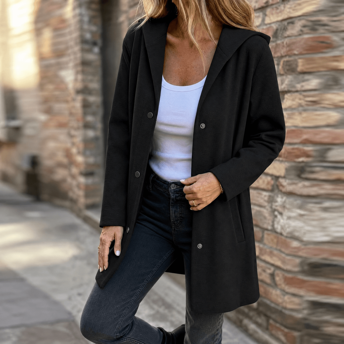 Black hooded longline cardigan worn open over a white top, with front buttons and patch pockets.