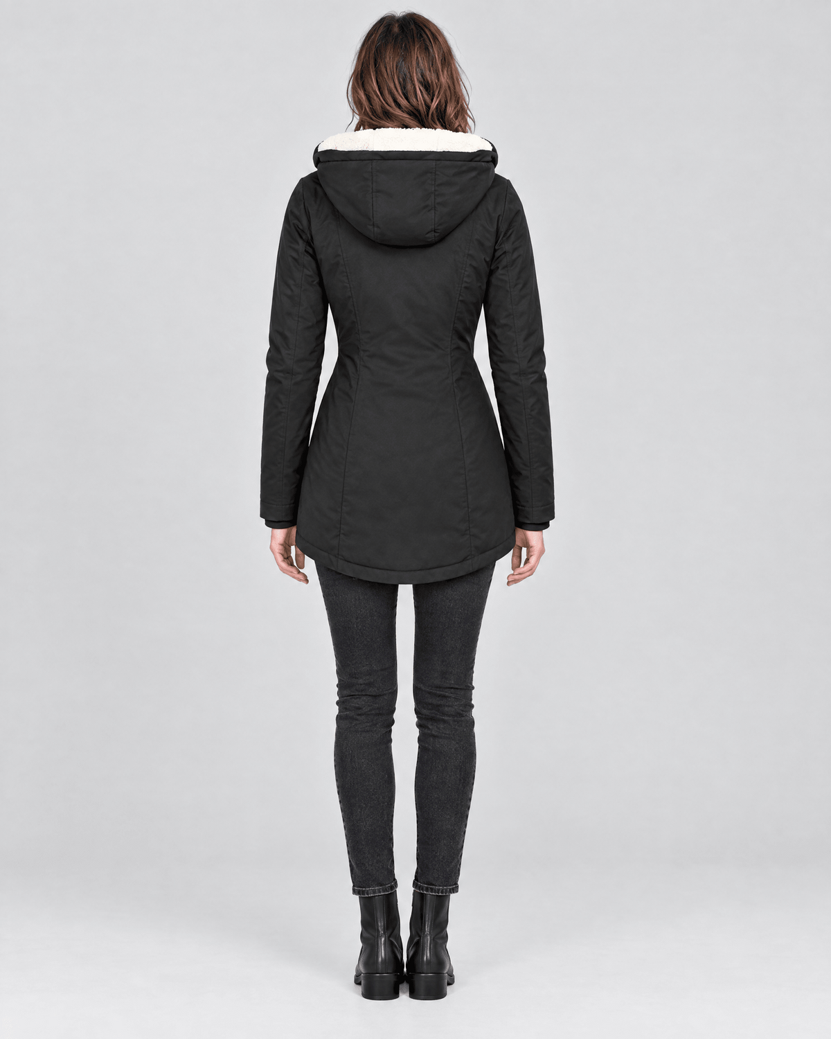Back view of the black jacket showing the attached hood, shaped waist, long sleeves, and rounded mid-length hem.