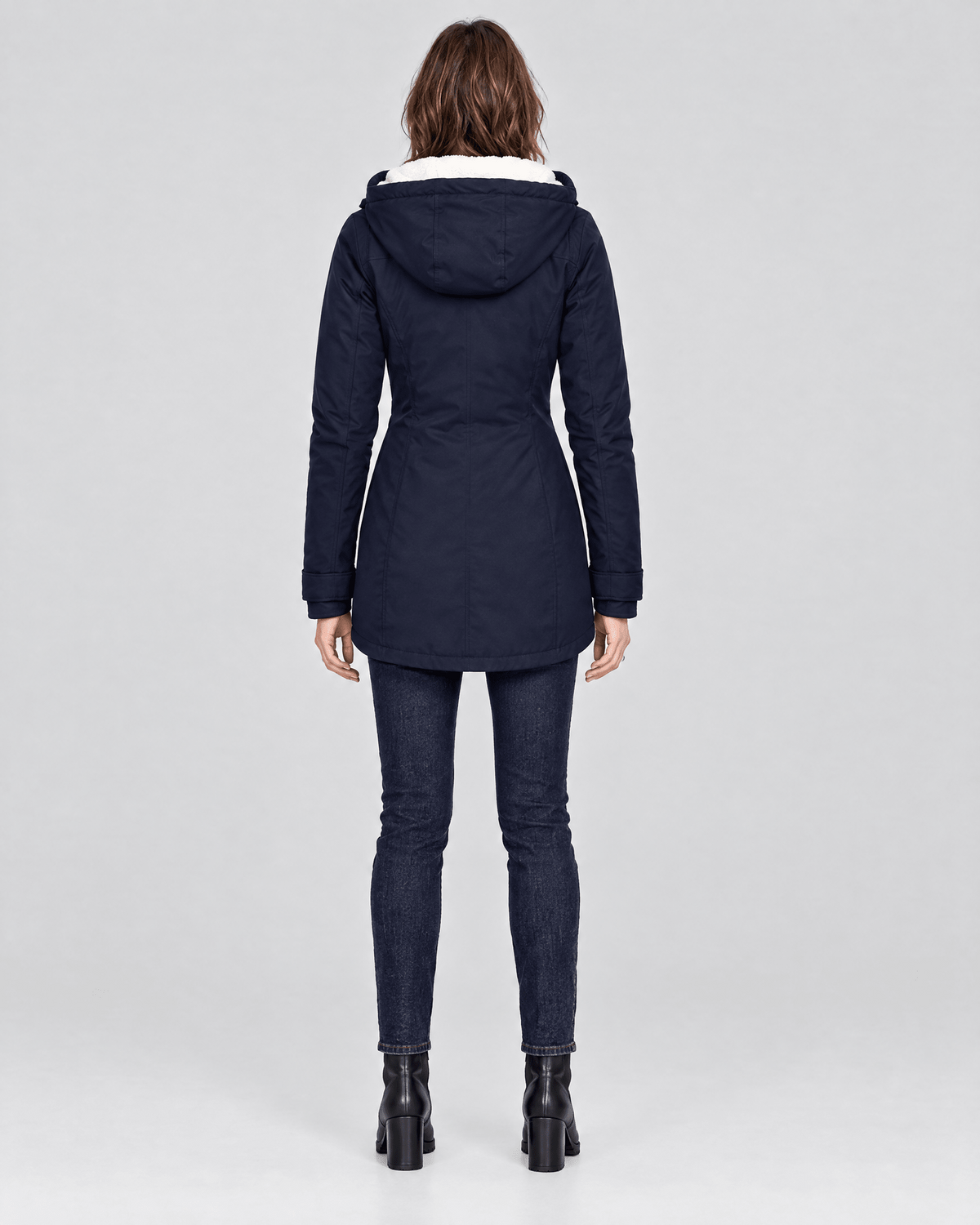 Back view of the navy jacket showing the hood, fitted waistline, long sleeves, and curved lower hem.