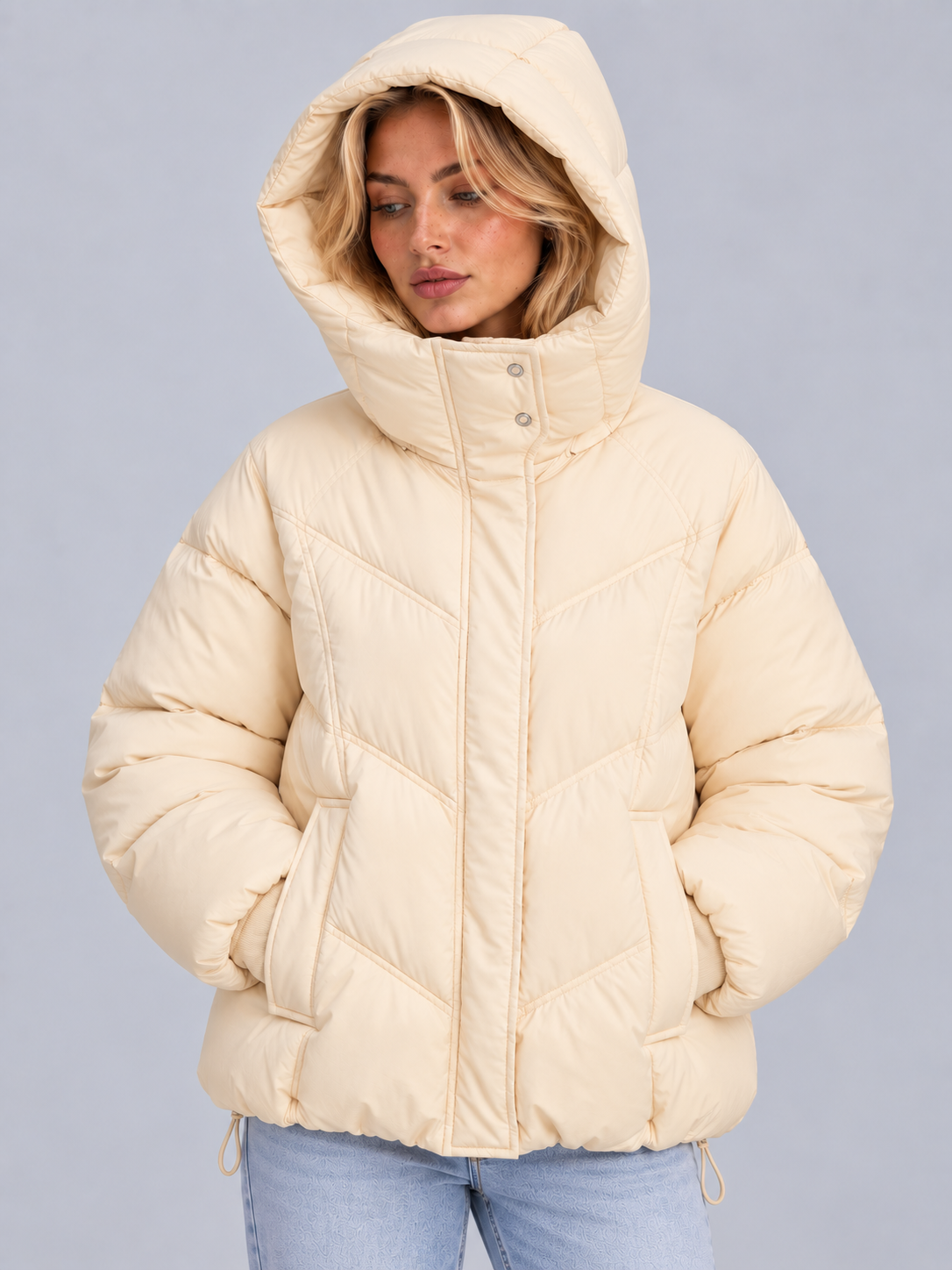 Front view of the cream puffer jacket worn with the hood raised and both hands tucked into its front pockets.