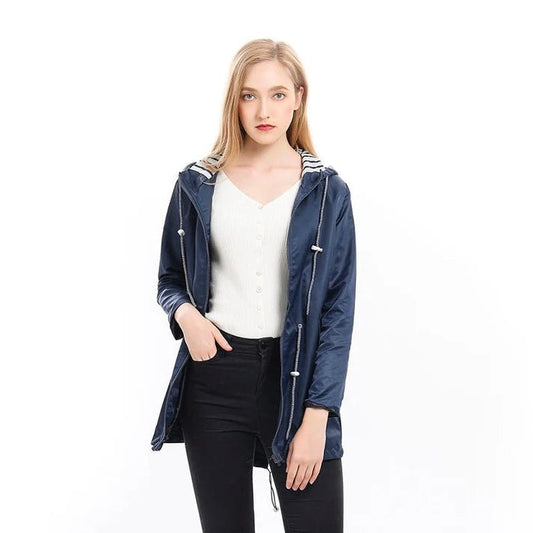 Model wearing a navy hooded raincoat open over a light top, showing the long sleeves, front zip, and drawstring waist.