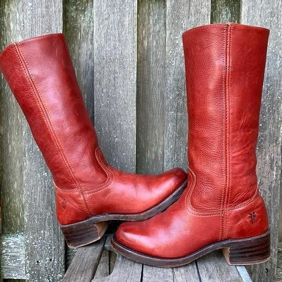Red knee-high boots arranged outdoors against a weathered wooden background, with one boot upright and the other angled across it.