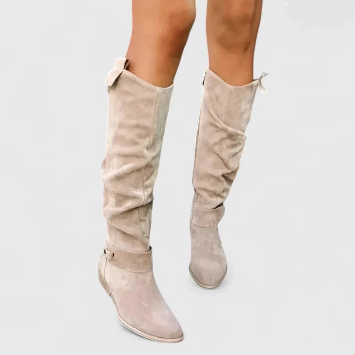 Light beige knee-high boots shown from the front, highlighting their rounded toes, relaxed ruched shafts, ankle straps, and low block heels.