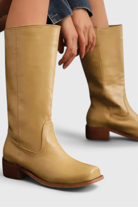 Tan knee-high boot with a rounded toe and low dark block heel, shown worn with a second boot behind it.