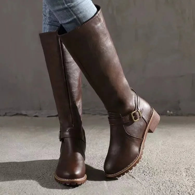 Brown knee-high riding boots shown at an angled view, with one boot lifted to reveal the ankle buckle and low heel.