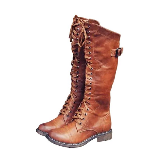 Brown knee-high riding boots with full front lacing, metal eyelets, side buckle straps, rounded toes, low block heels, and flat soles.