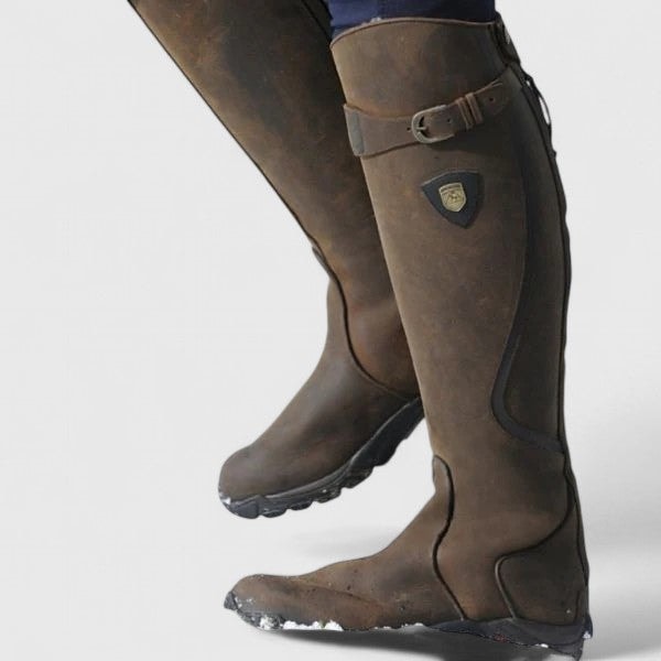 Brown knee-high riding boots shown close up, highlighting the adjustable buckle strap, curved panel stitching, rounded toe, and textured outsole.