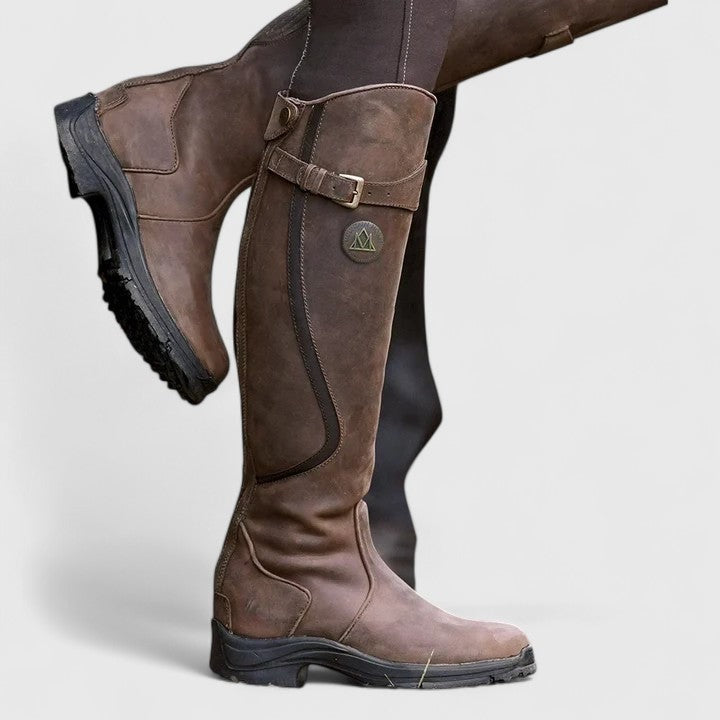 Brown knee-high riding boots displayed at an angle, showing the tall shaft, side zip, buckle detail, rounded toe, and low block heel.
