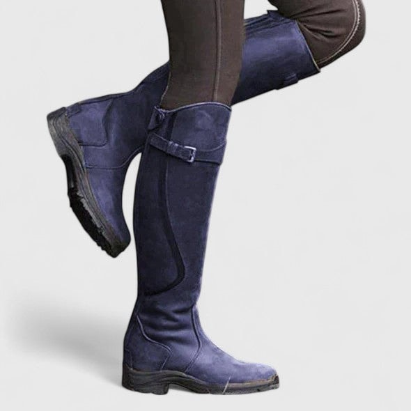 Navy knee-high riding boots worn with dark leggings, showing the side buckle, fitted shaft, rounded toe, and practical low heel.