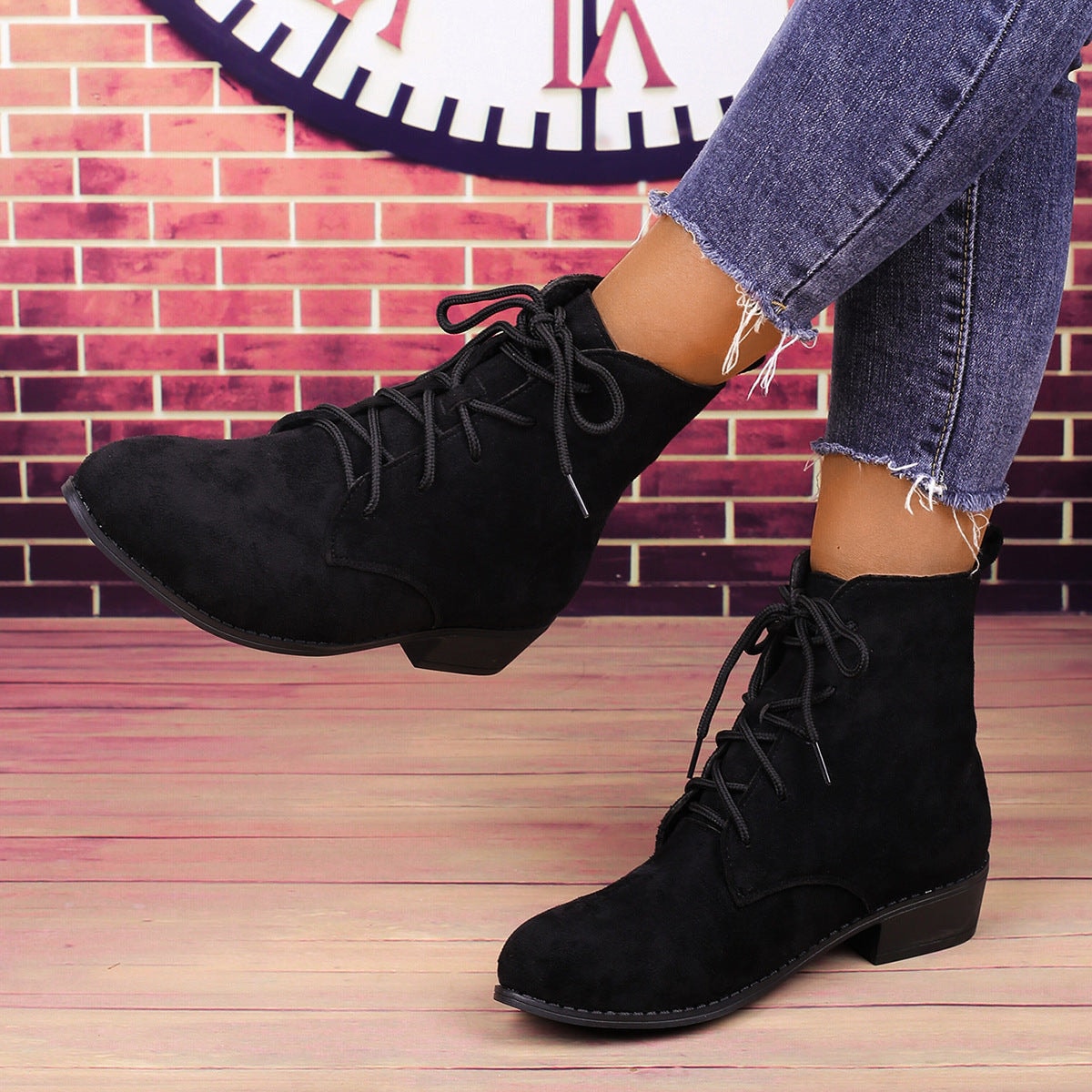 Black lace-up ankle boots shown worn in a walking pose, with one boot lifted to reveal the low block heel and sole.
