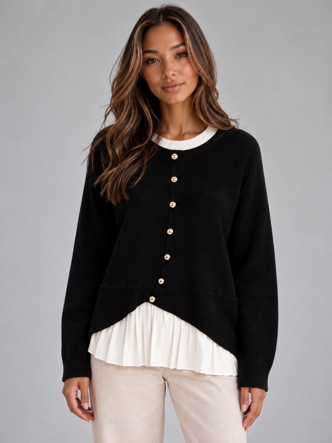 Front view of a black women's layered cardigan with a white crew neckline, button front, long sleeves, curved hem, and pleated white shirt-style panel.