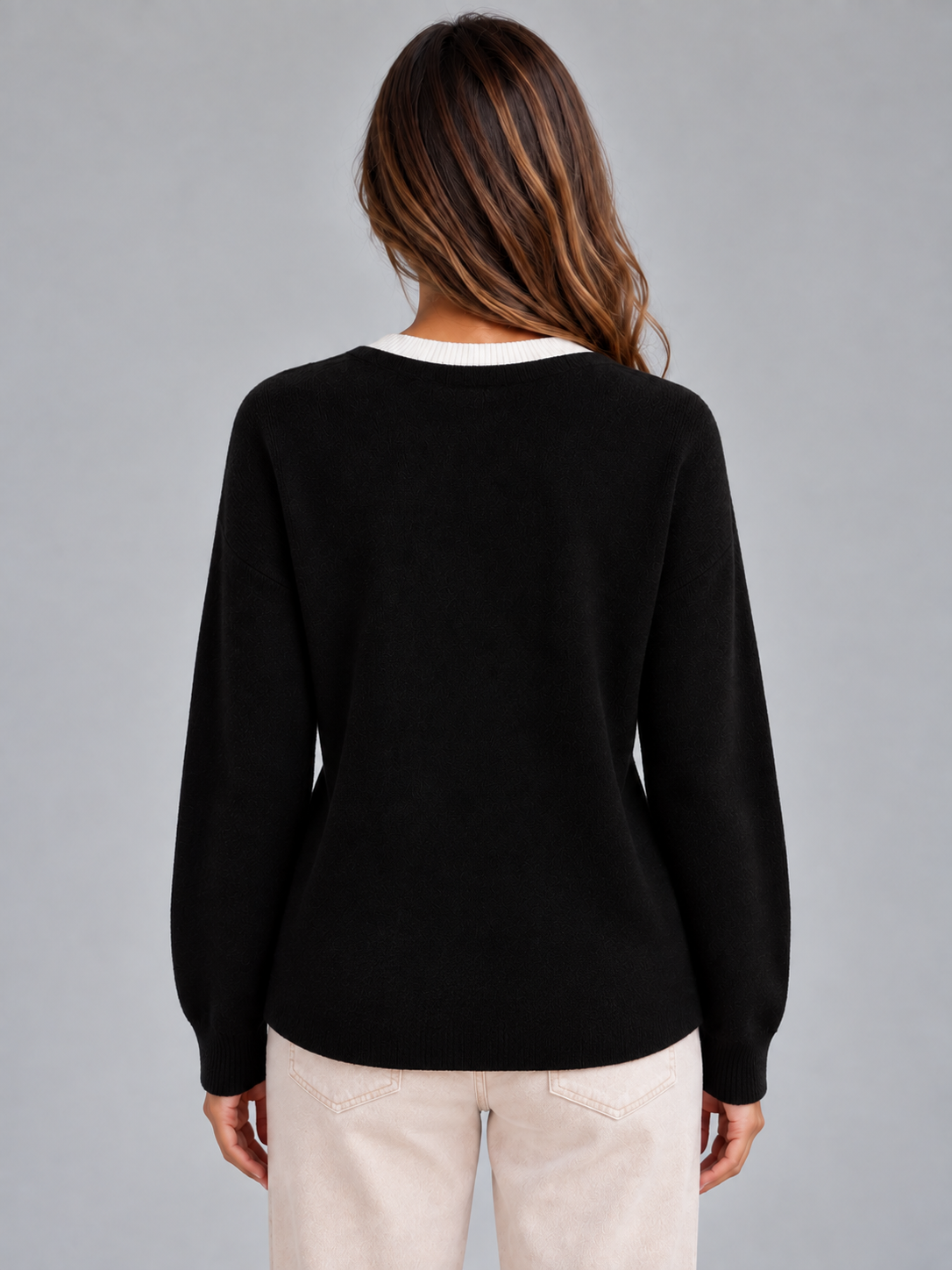 Back view of the black layered cardigan, showing its plain back, long sleeves, ribbed cuffs, and curved lower hem.
