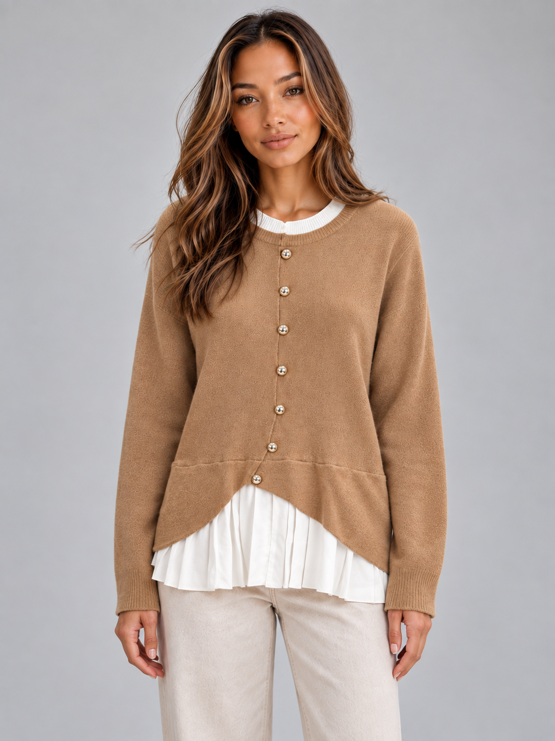 Front view of the layered cardigan in tan, featuring a white crew neckline, button front, curved hem, and pleated white lower panel.