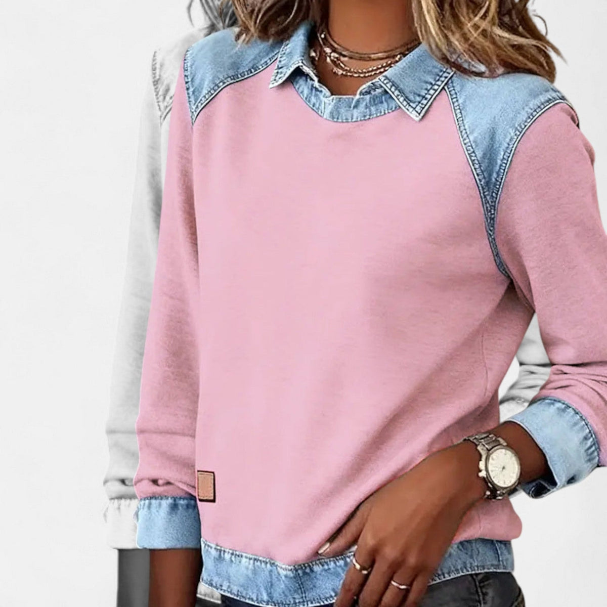 Angled view of the pink layered-collar sweater showing the relaxed body and blue lower hem panel.