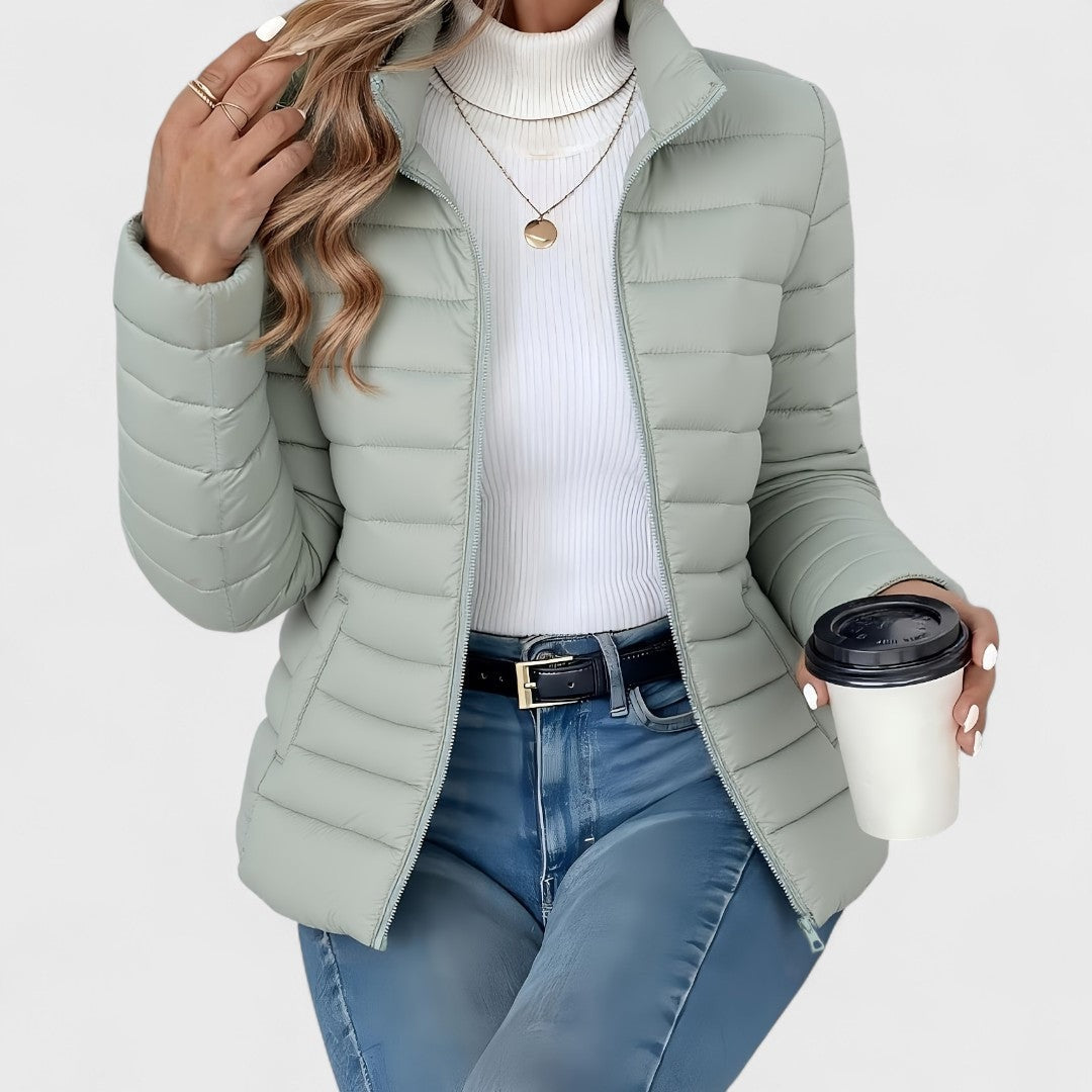 Light sage quilted jacket with a stand collar, long sleeves, and open full-length zipper styled over a white turtleneck.