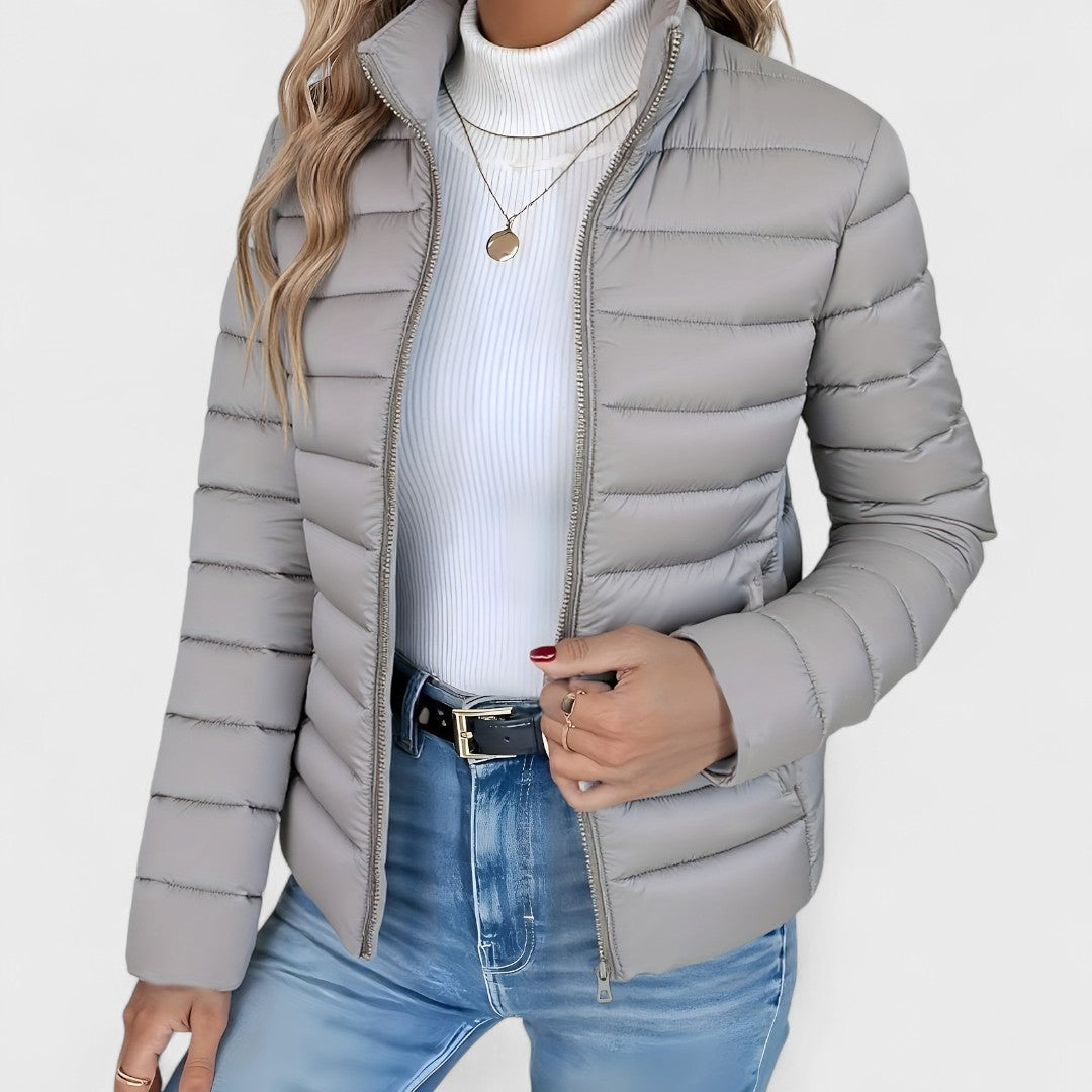 Light gray quilted jacket shown nearly zipped, with horizontal quilting, a stand collar, and long sleeves.