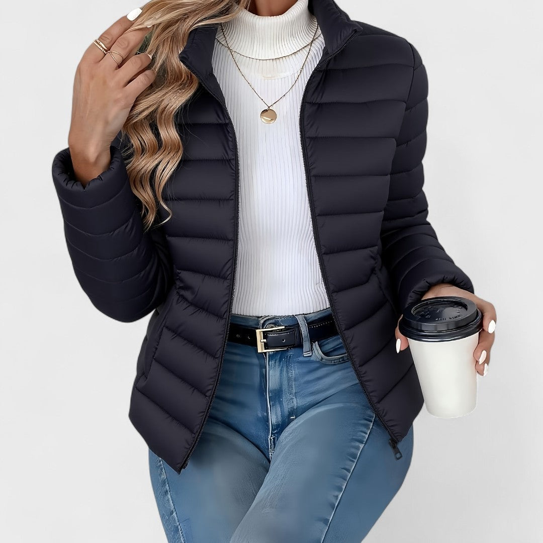 Dark navy quilted jacket with a stand collar and open front, paired with jeans and a white turtleneck.